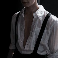 a man wearing suspenders and a white shirt is standing in the dark with his hands on his hips