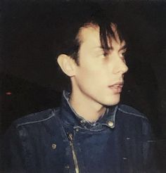 a young man wearing a denim jacket looks off into the distance