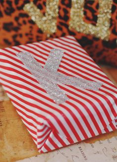 a red and white striped paper bag with a cross on the front sitting next to a leopard print purse