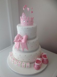 a three tiered cake decorated with pink and white fondant, baby booties and tiara