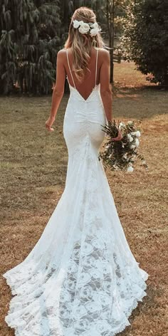 a woman in a wedding dress is walking through the grass with her back to the camera