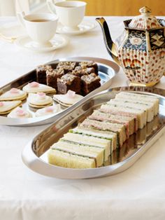 two trays filled with sandwiches and pastries on top of a white table cloth