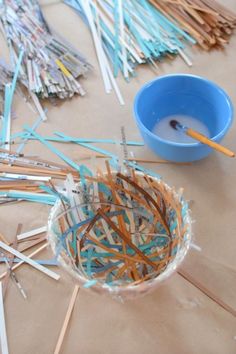 a blue bowl filled with sticks sitting on top of a table next to a cup