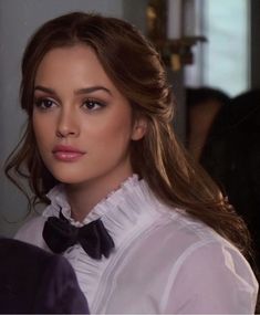 a woman with long hair wearing a white shirt and bow tie looking at the camera