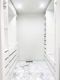 an empty walk in closet with white walls and marble flooring on one side, open shelving unit to the other