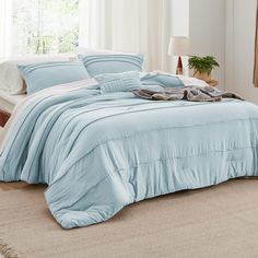 a bed with blue comforter and pillows in a white room next to a window