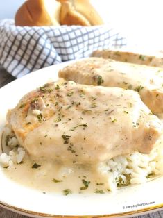 chicken with gravy and rice on a white plate next to bread in the background