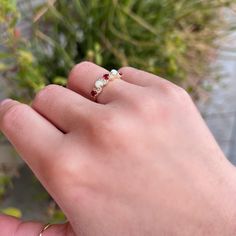 a person's hand with a ring on their finger and flowers in the background