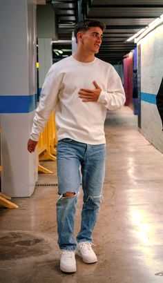 a man walking down a hallway with his hand on his hip while wearing ripped jeans