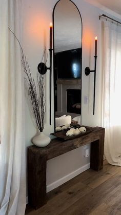 a mirror and some candles on a table in front of a window with white curtains