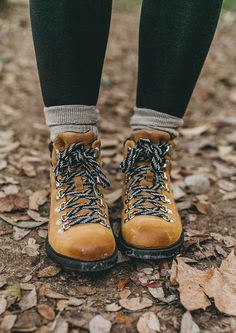 the legs and feet of a person wearing yellow hiking boots on leaves in front of them