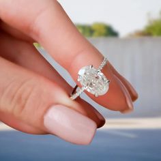 a woman's hand holding an engagement ring in front of her face with the diamond on it