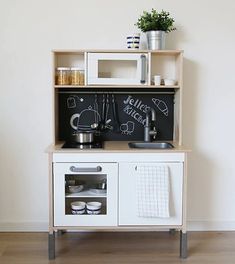 a white wooden play kitchen with chalkboard on the wall and pots, pans and utensils