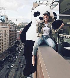 a woman sitting on top of a building next to a giant stuffed animal panda bear