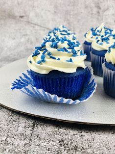 three blue cupcakes with white frosting and sprinkles on a plate