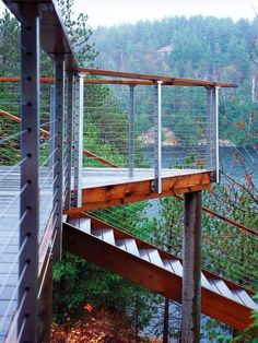 a wooden walkway with metal railings leading to a body of water and trees in the background