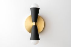 two black and gold sconces on a white wall, one with a light bulb