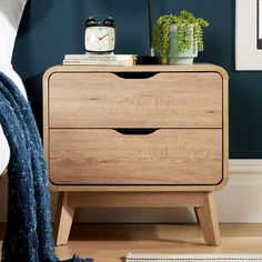 a night stand with two drawers and a clock on the top, next to a bed