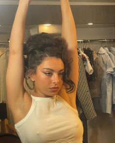 a woman in a white tank top is holding her arms above her head