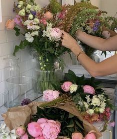 a woman is arranging flowers in a vase on the counter with other flowers and greenery