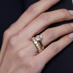 a woman's hand with a gold ring and diamond engagement ring on her finger