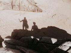 two people are standing on rocks in the sand and one person is holding his hand out