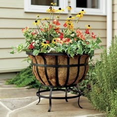 a planter filled with lots of flowers sitting on top of a stone floor next to a house