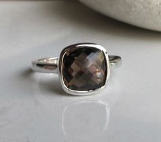 "A stunning sterling silver ring featuring a cushion shaped faceted Smoky Quartz makes a classic ring for any occasion. Wrapped in a box ready for gift giving.(r-nc-127) The lovely Smoky Quartz measure 9mm Also Available in Matching Smoky Quartz Stud Earring https://www.etsy.com/listing/185974813/sale-smoky-quartz-studs-silver-studs?ref=shop_home_active_21 *Follow us @belesasjewels on instagram for promotions/giveaways *LIKE* us on Facebook http://www.facebook.com/Belesas to find special coupon Classic Stackable Topaz Ring As Gift, Classic Stackable Topaz Ring Gift, Modern Cushion Cut Rings For Gift, Elegant Faceted Stackable Rings, Classic Faceted Topaz Ring As Gift, Classic Cushion Cut Topaz Ring Gift, Elegant Faceted Stackable Sterling Silver Rings, Elegant Sterling Silver Faceted Stackable Rings, Classic Faceted Topaz Ring For Gift