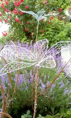 a wire dragon sitting on top of a lush green field next to purple and red flowers