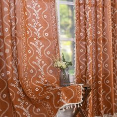 a vase with flowers sitting on top of a wooden table next to a curtained window