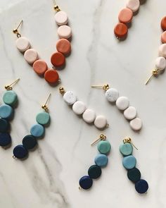 six pairs of earrings with different colors and shapes on them sitting on a marble surface