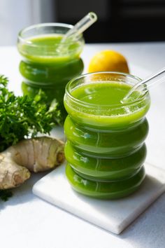 two glasses filled with green liquid sitting on top of a cutting board