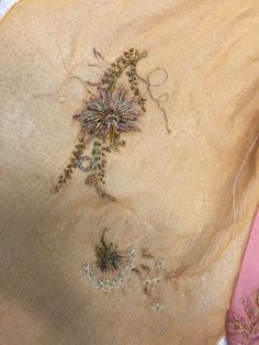 an embroidered piece of cloth with flowers on it next to some thread and needles in the background