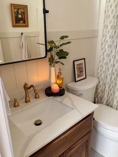 a white toilet sitting next to a bathroom sink under a mirror with a candle on it