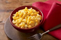 a red bowl filled with macaroni and cheese on top of a wooden table