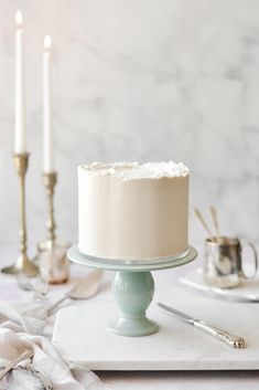 a white cake sitting on top of a table next to two silver candles and napkins