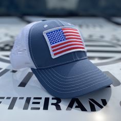 Slate & White Mesh-Back Trucker Hat Custom Made Right Here In The USA! 🇺🇸 This slate fabric and white mesh trucker hat has an oversized full-color American flag and branded side panel. ✅ Our classic trucker hats are structured with a higher profile ✅ Pre-curved visor ✅ Snap-back closure ✅ Branded side panel ✅ Moisture-wicking sweatband ✅ Classic top button ✅ Superior quality, comfort, and American craftsmanship. White Cap For Memorial Day, Patriotic White Snapback Trucker Hat, White Americana Hat With Adjustable Fit, Patriotic White Snapback Baseball Cap, Patriotic White Trucker Hat/baseball Cap, White Country Style Trucker Hat With Curved Brim, Patriotic White Baseball Cap With Curved Bill, Country Style White Snapback Hat, White Patriotic Hat With Curved Bill