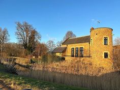 an old brick building sitting on the side of a road next to tall grass and trees