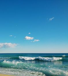 an ocean view with waves crashing on the shore and blue sky in the back ground