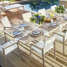 an outdoor dining table with white chairs and plates on it next to a swimming pool