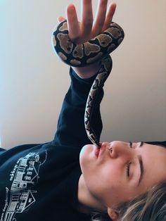 a woman laying on top of a bed holding a snake up to her face with both hands