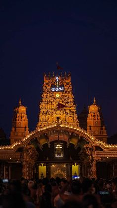 people are standing in front of an ornate building with lights on it at night time