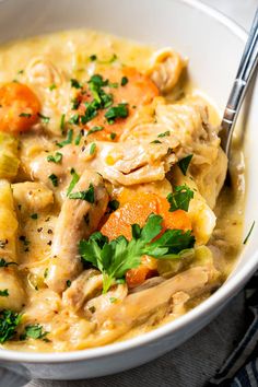 a white bowl filled with chicken, carrots and dumplings next to a fork