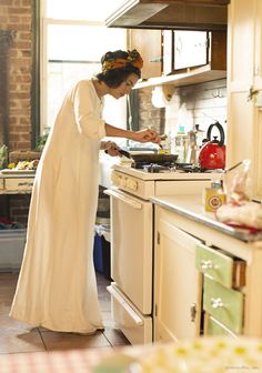 a woman in a white dress is preparing food on the stove and she is wearing a headband