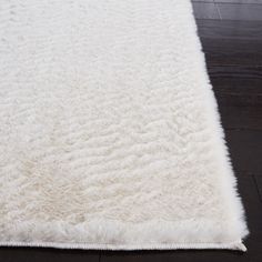 a large white rug on top of a wooden floor with dark wood floors in the background