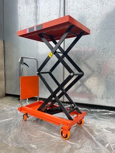 an orange scissor sitting on top of a plastic tarp next to a wall