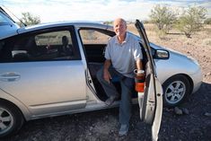 a man sitting in the open door of a silver car