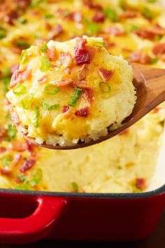 a spoon full of mashed potatoes in a red casserole dish with bacon and green onions