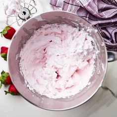 a metal bowl filled with whipped cream next to strawberries on a white counter top