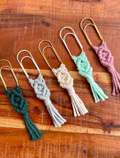 four different colored tassels are on a wooden surface with metal hooks and paper clips